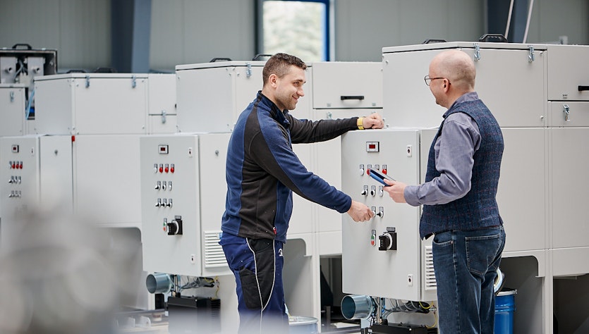 Two men tals to each other in front of a ventilation system