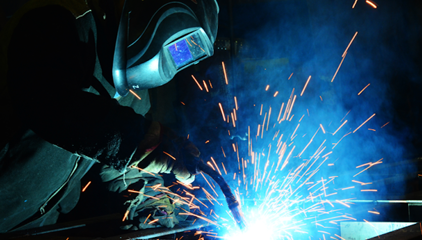 Person with helmet is welding a metal plate surrounded by sparks